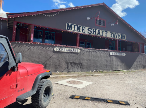 Exterior of the Mine Shaft Tavern with a red Jeep parked in front, featuring signs for restaurant and cocktails.